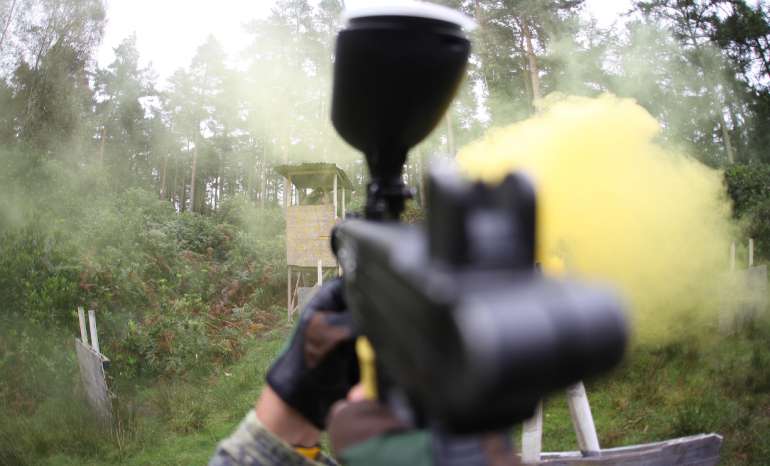 A person is seen with a paintball gun, emitting a cloud of yellow smoke, capturing a moment of thrilling activity